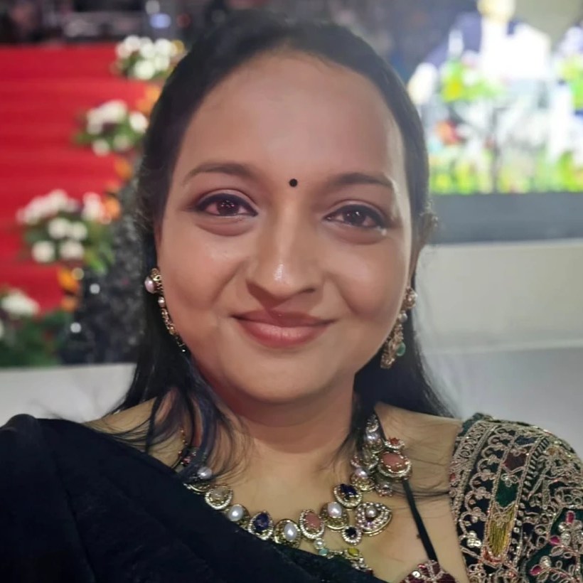 Dr Lavanya smiling at a stage event, wearing a black velvet saree and jewelled necklace